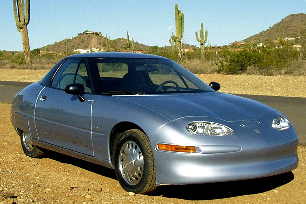 Une GM EV1 de 1996, voiture électrique aérodynamique et futuriste, garée sur une rue moderne sous un ciel bleu.