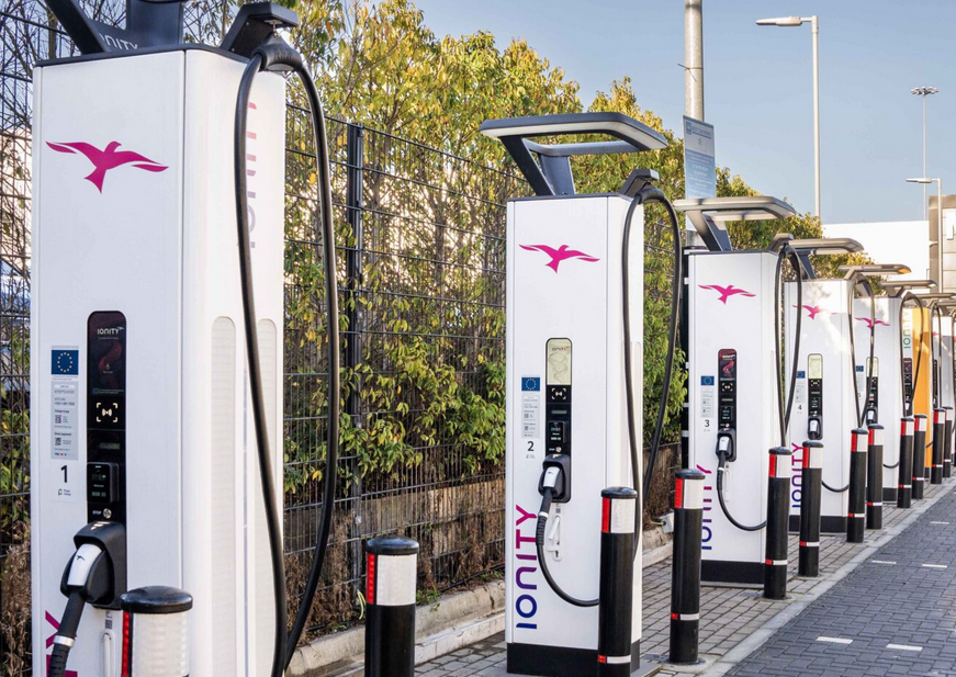 Vue d'une station de recharge Ionity moderne avec plusieurs bornes de recharge et des véhicules électriques en charge, située sur une aire d'autoroute française.
