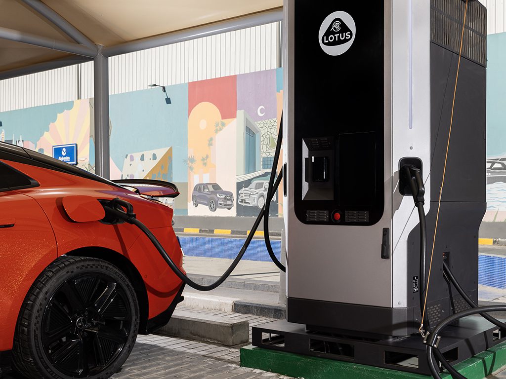 Une Lotus Emeya noire et élégante connectée à une borne de recharge Ionity, avec le câble de recharge visible et d'autres véhicules électriques en arrière-plan.