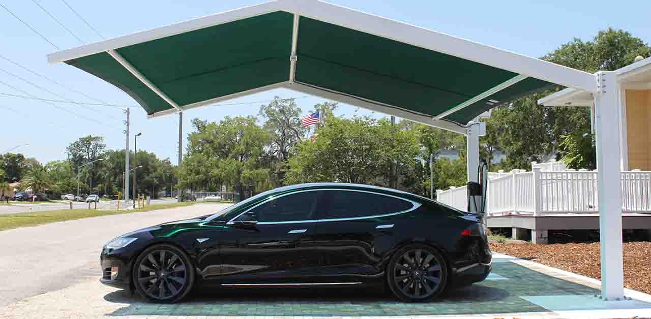 Une voiture électrique en train de charger à l'ombre d'un arbre ou d'un parking couvert, sous un soleil éclatant.