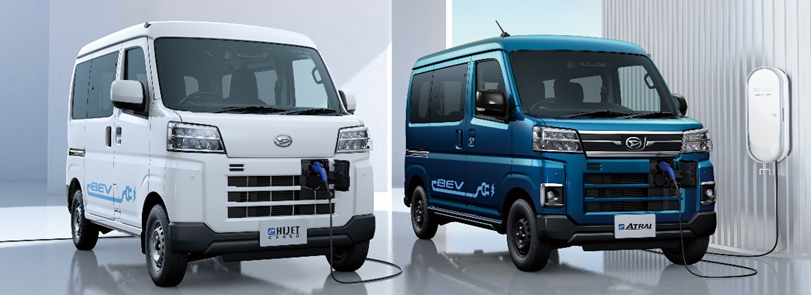 Un mini-van électrique Daihatsu e-Hijet Cargo en train de recharger à une borne CHAdeMO dans un environnement urbain animé.