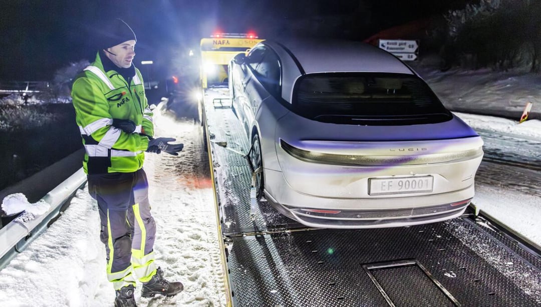 Une Lucid Air Grand Touring blanche roule sur une route enneigée et glacée en Norvège, avec des montagnes enneigées en arrière-plan sous un ciel hivernal clair.