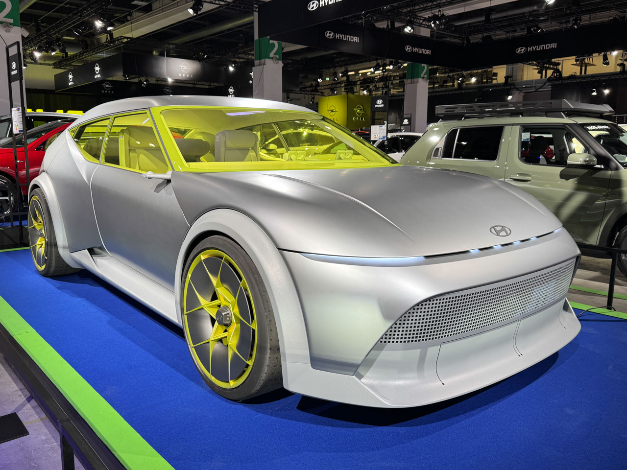 Une Hyundai Ioniq 3 argentée, au design futuriste, garée dans une rue urbaine moderne, ses phares distinctifs allumés.