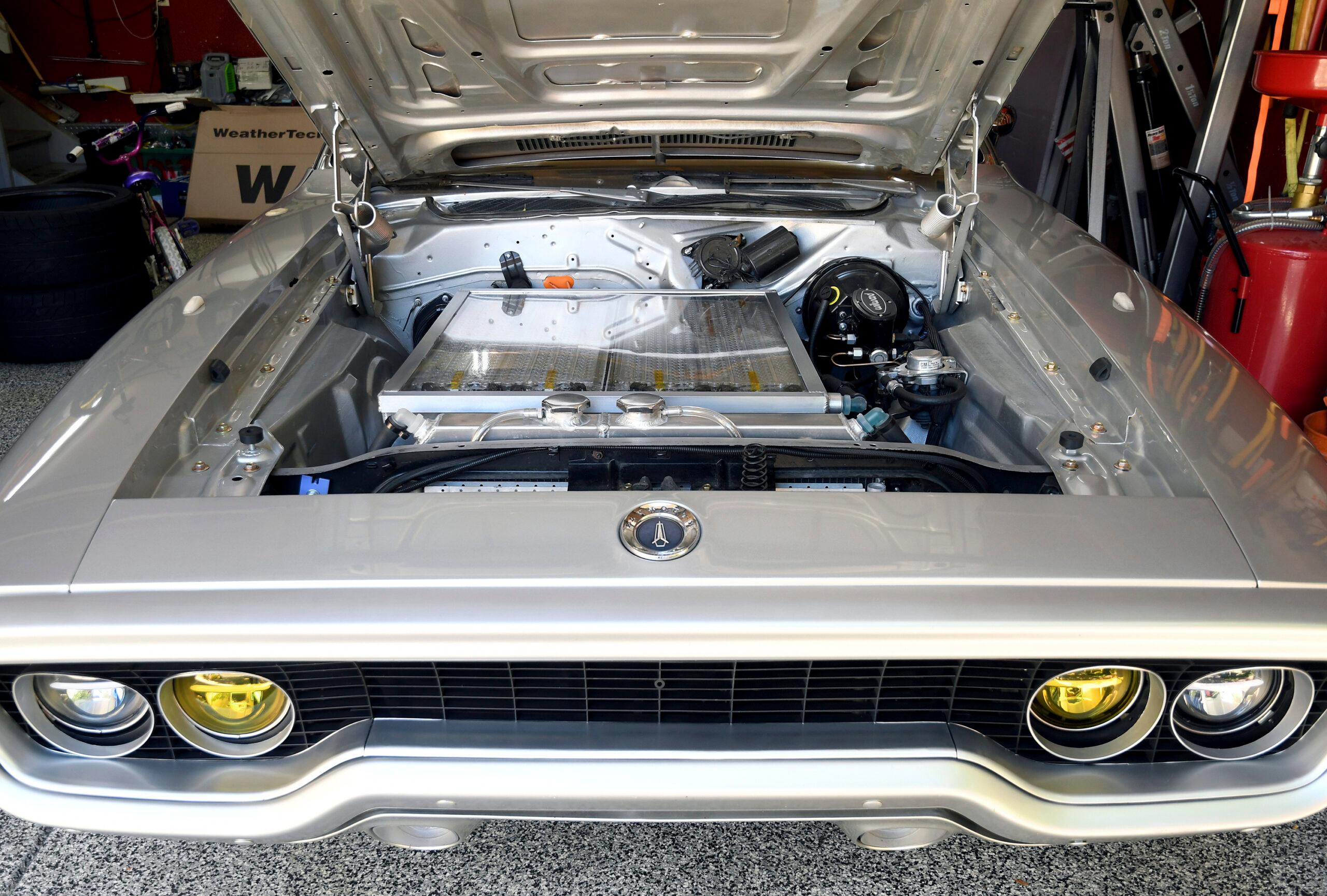 Vue détaillée d'une vieille voiture en cours de conversion électrique dans un atelier, avec le moteur thermique retiré et un moteur électrique en cours d'installation.