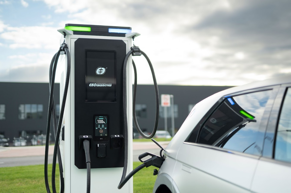 Image d'une voiture électrique branchée à une borne de recharge, avec des lumières urbaines en arrière-plan.