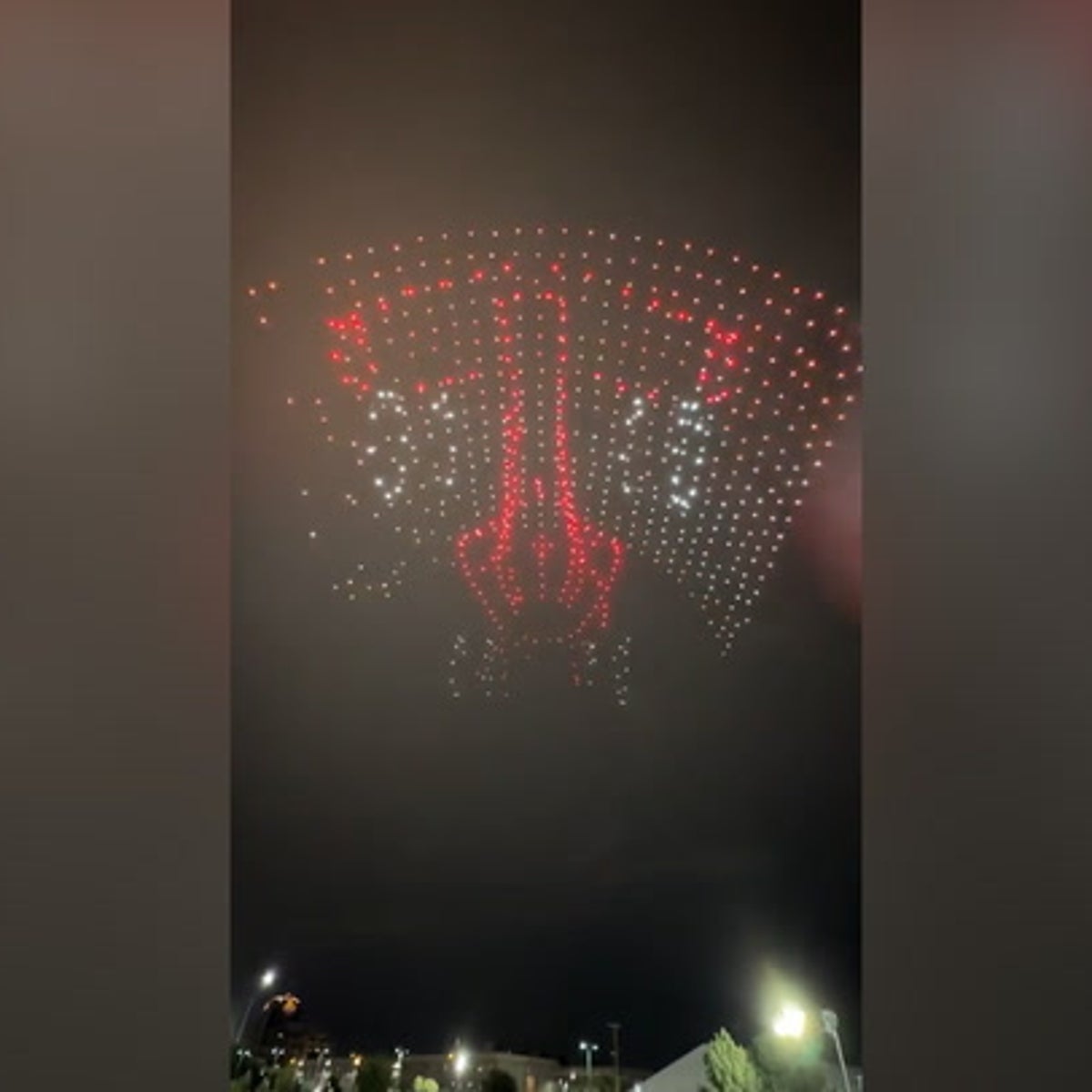 Un spectacle de drones nocturne où des centaines de drones lumineux créent un logo de voiture dans le ciel, au-dessus de voitures exposées.