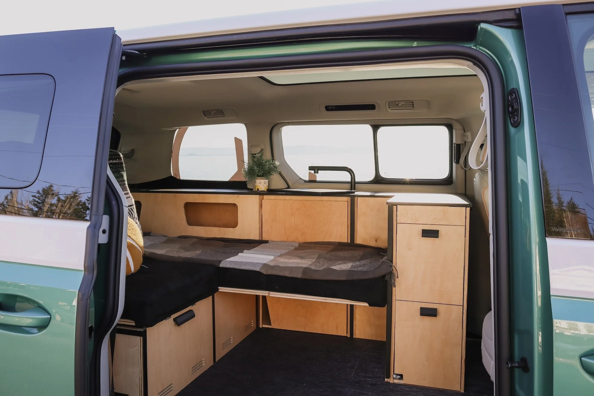 Vue intérieure d'un VW ID.Buzz transformé en camping-car par Peace Vans, avec un coin cuisine compact, un lit et des rangements intégrés.