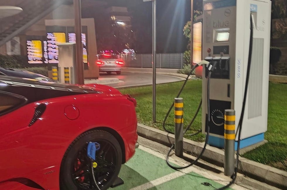 Une Ferrari électrique élégante en train de charger à une station de recharge futuriste, dans un environnement urbain sophistiqué.