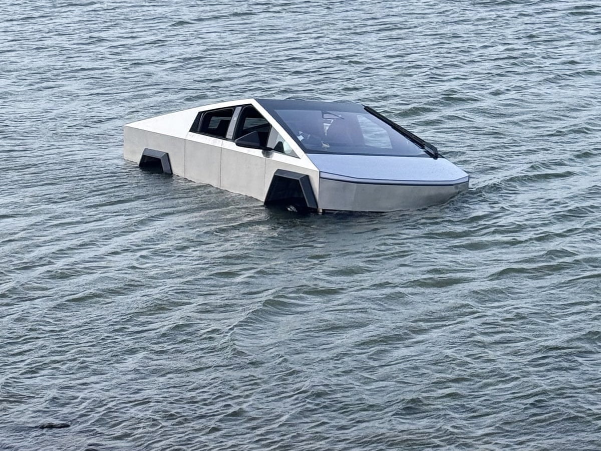 Un Tesla Cybertruck gris, au design angulaire, est à moitié submergé dans un lac. Des secouristes sont visibles en arrière-plan.